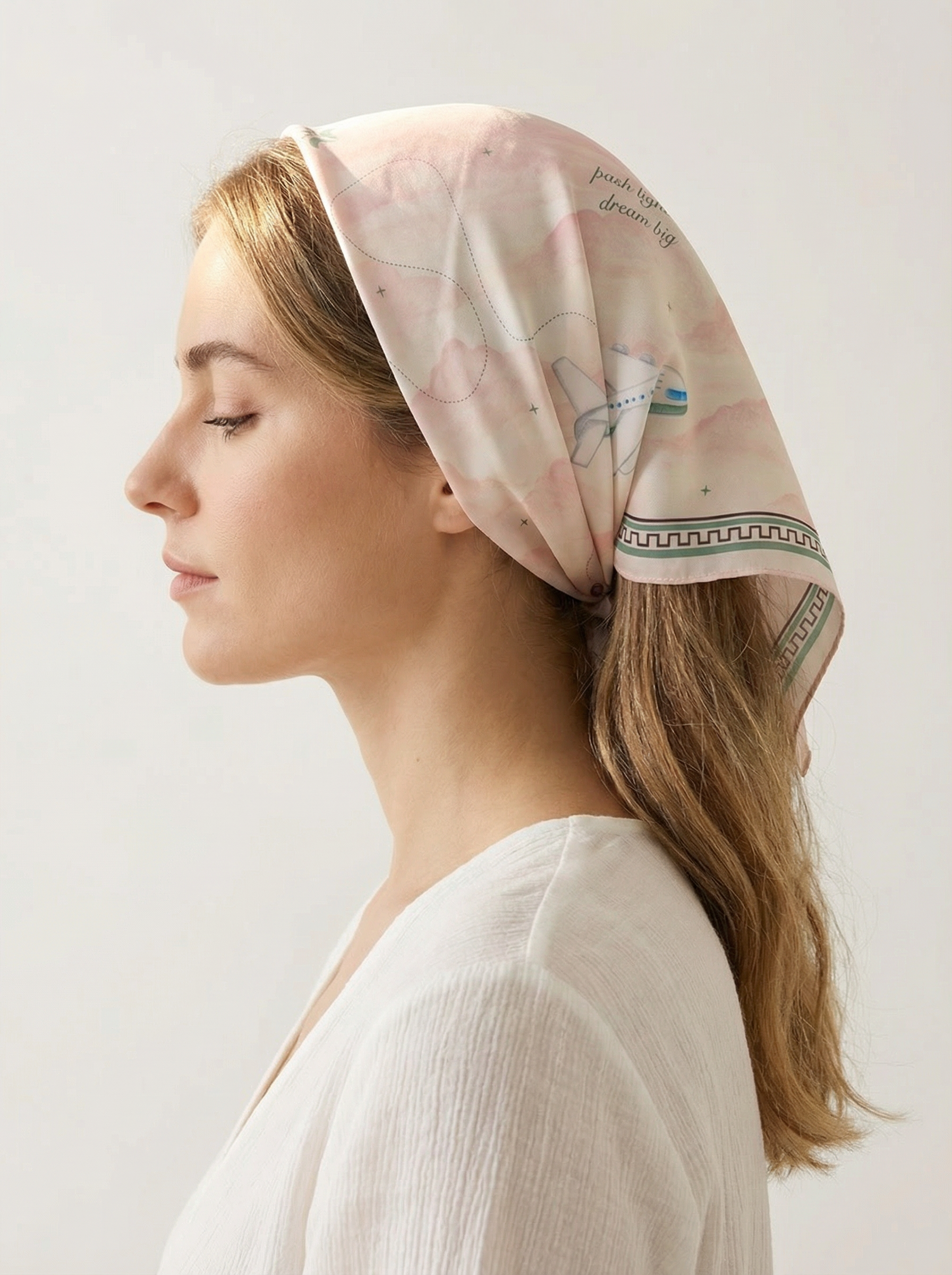Woman wearing a headscarf with airplane design and text on a plain background